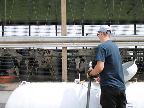 A Renway driver filling a farm tank beside a dairy barn